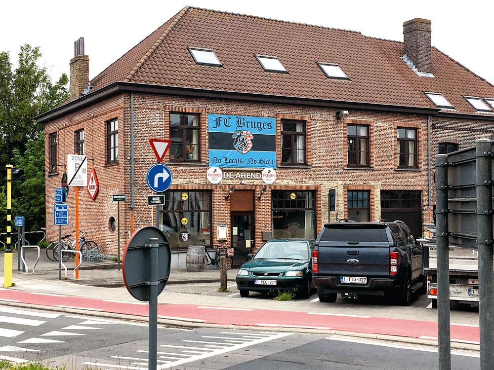 Boven de deur van café Den Arend hangt een vlag: FC Bruges. No Locals/No Glory.