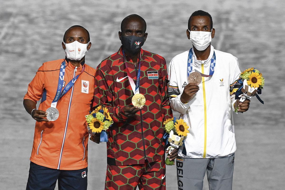 Abdi Nageeye (à gauche) et Bashir Abdi (à droite) entourent le médaillé d'or du marathon Eliud Kipchoge lors de la remise des médailles lors des JO de Tokyo.