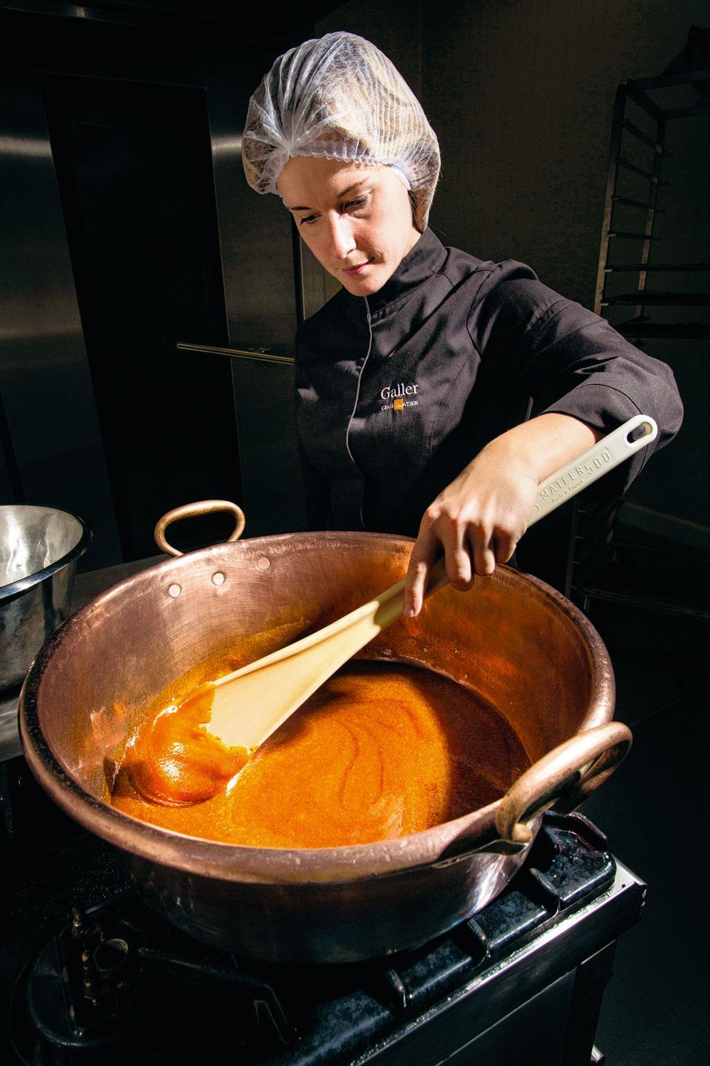 De vulling bereiden - Voor de bereiding van de nieuwe praline met karamel en pecannotenwordt eerst karamel gemaakt door de suiker te verhitten in een grote koperen ketel en die geregeld behoedzaam om te roeren. 