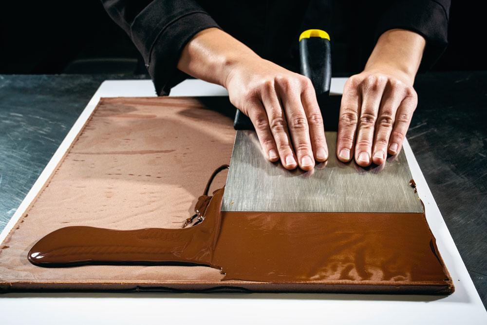 Versnijden - Nadat de 'pralineplaten' gedurende 24 uur hebben gerust en een zijn keer met chocolade werden overgoten, worden ze met behulp van een snijmachine versneden tot 256 pralines. De pralines zijn nu klaar voor de laatste fase in het productieproces.
