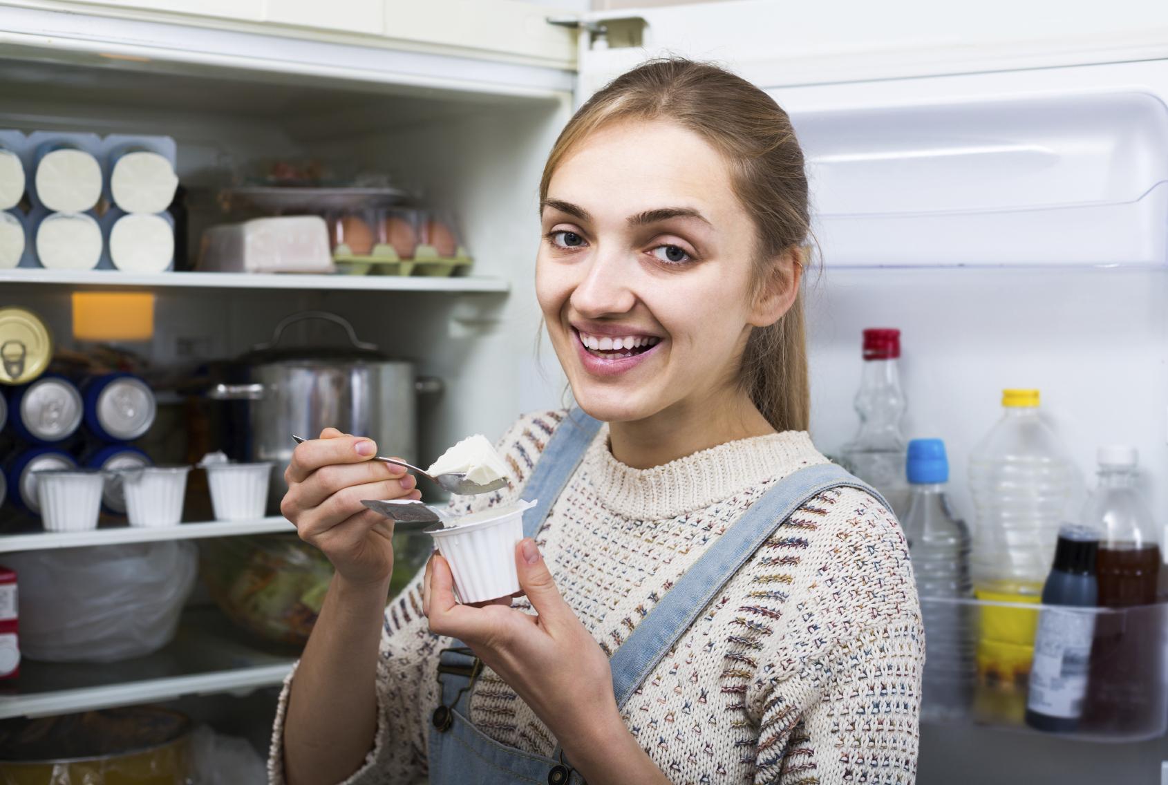 young brunette standing near fridge with soft cheese