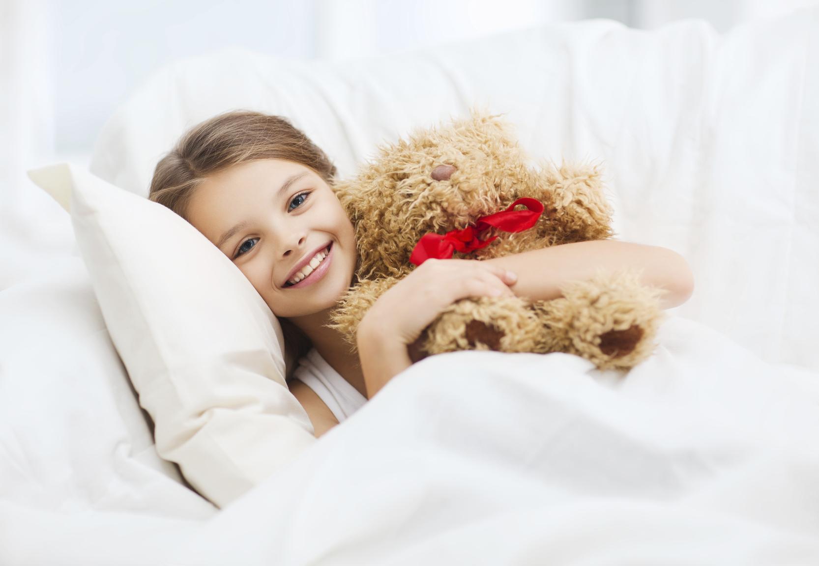 little girl with teddy bear sleeping in bed at home