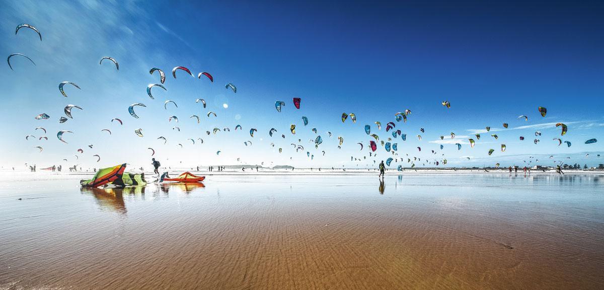 Een ballet van vliegers op het strand van Essaouira, Marokko. Je zou haast vergeten dat er surfers onder hangen.