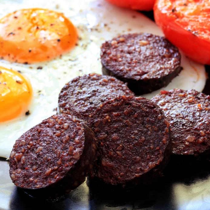 Breakfast of traditional black pudding, fried eggs and tomatoes.