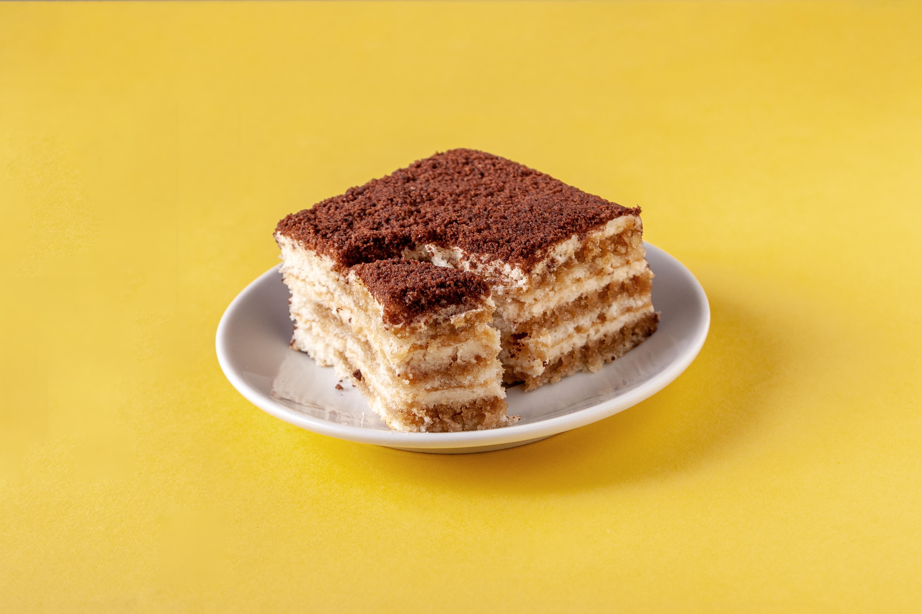 portion of tiramisu on a white plate on a yellow background