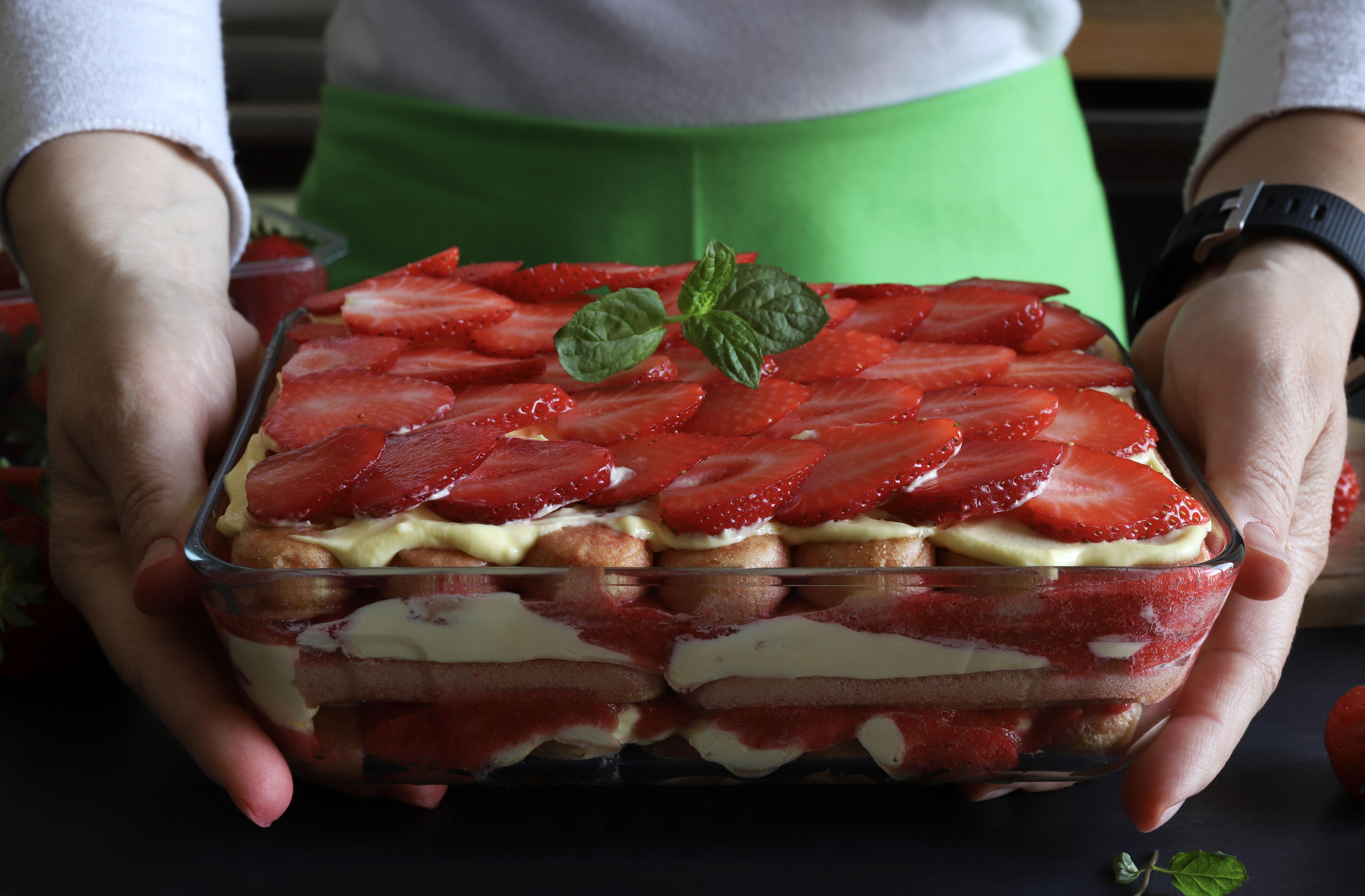 Homemade Italian dessert. Woman holding a glass tray with strawberry tiramisu. Closeup.