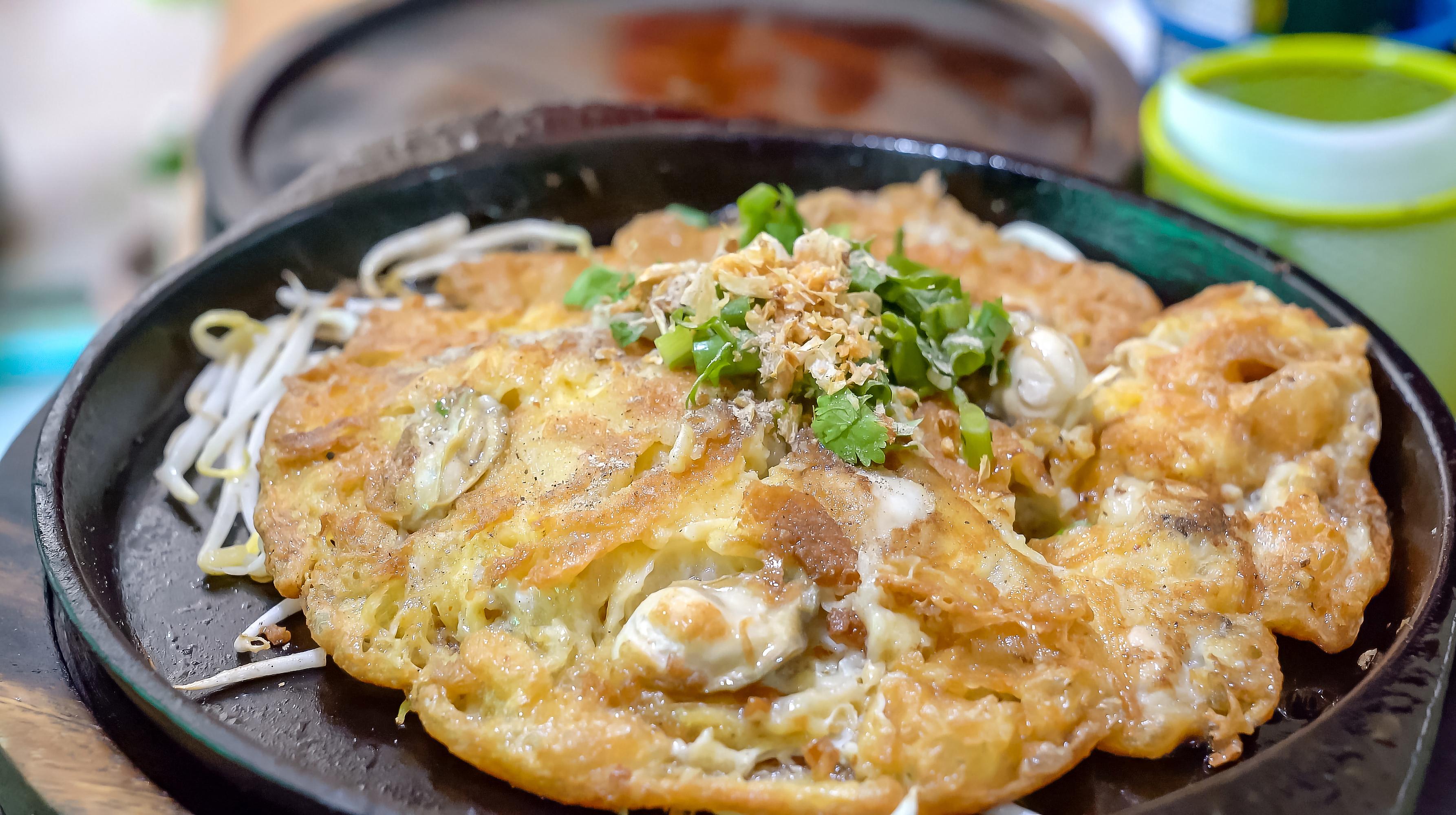 On a hot, black pan, a pan fried oyster omelet with bean sprouts. In the hot pan, this menu is ready to be served and consumed.