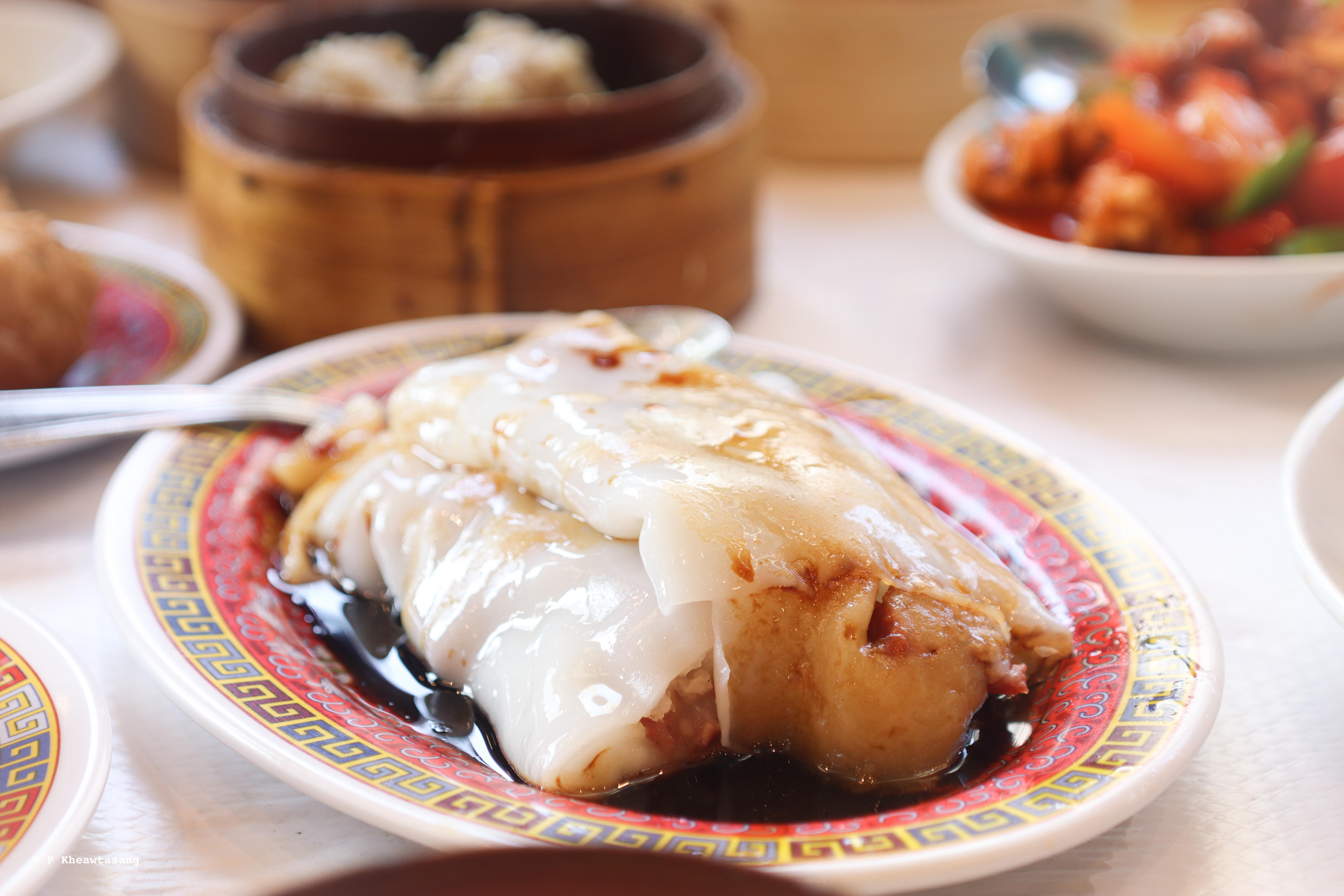 A plate of steamed rice noodle rolls or Cheung Fun in Chinese language. One of traditional Dim Sum, bamboo container in background. A Soft and tender sheets filled with sweet and savory roasted pork