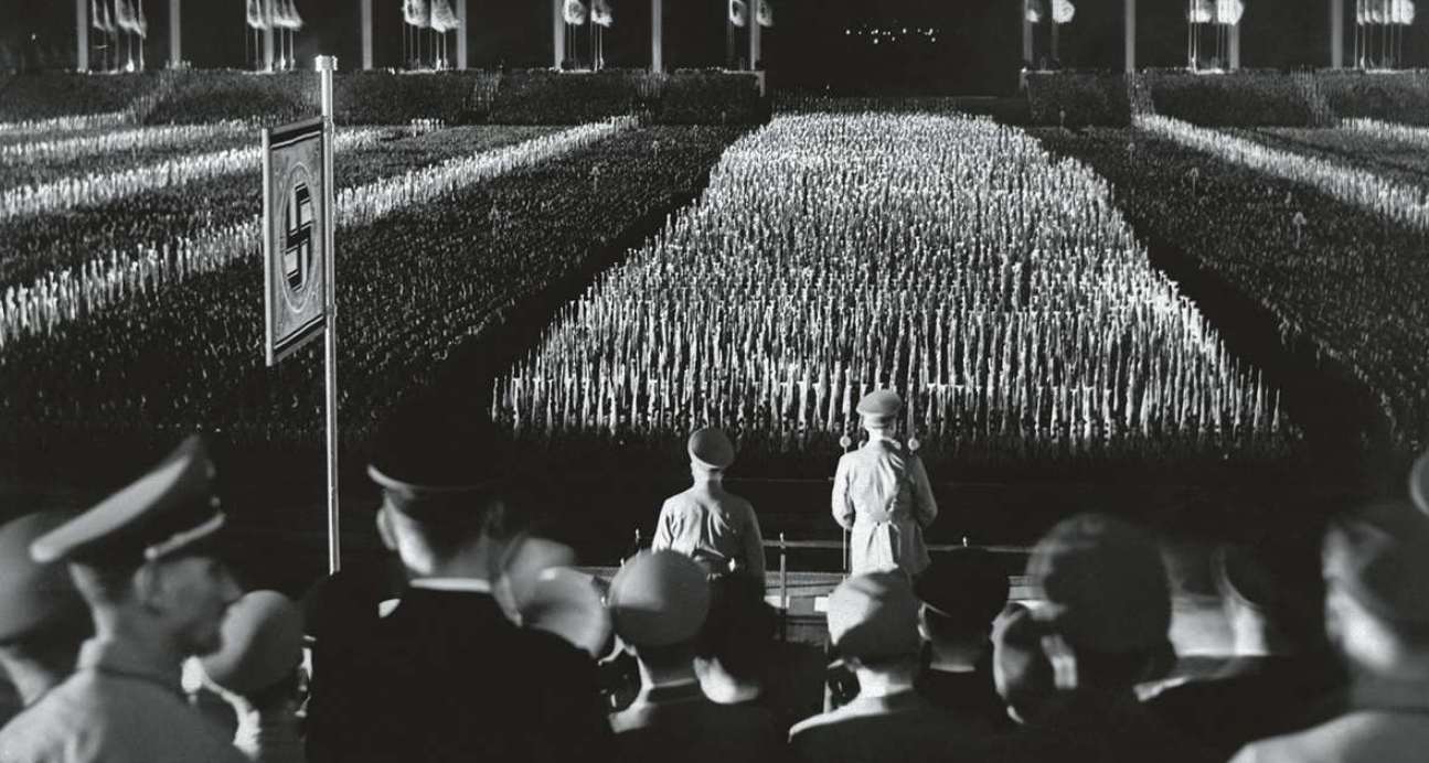 Foto: 9 december 1938: bondskanselier Hitler aan het woord op de jaarlijkse ralla van de nazi-partij in Neurenberg. Op de achtergrond zie je de theatrale ‘kathedraal van licht’, ontworpen door Albert Speer. © Getty Images