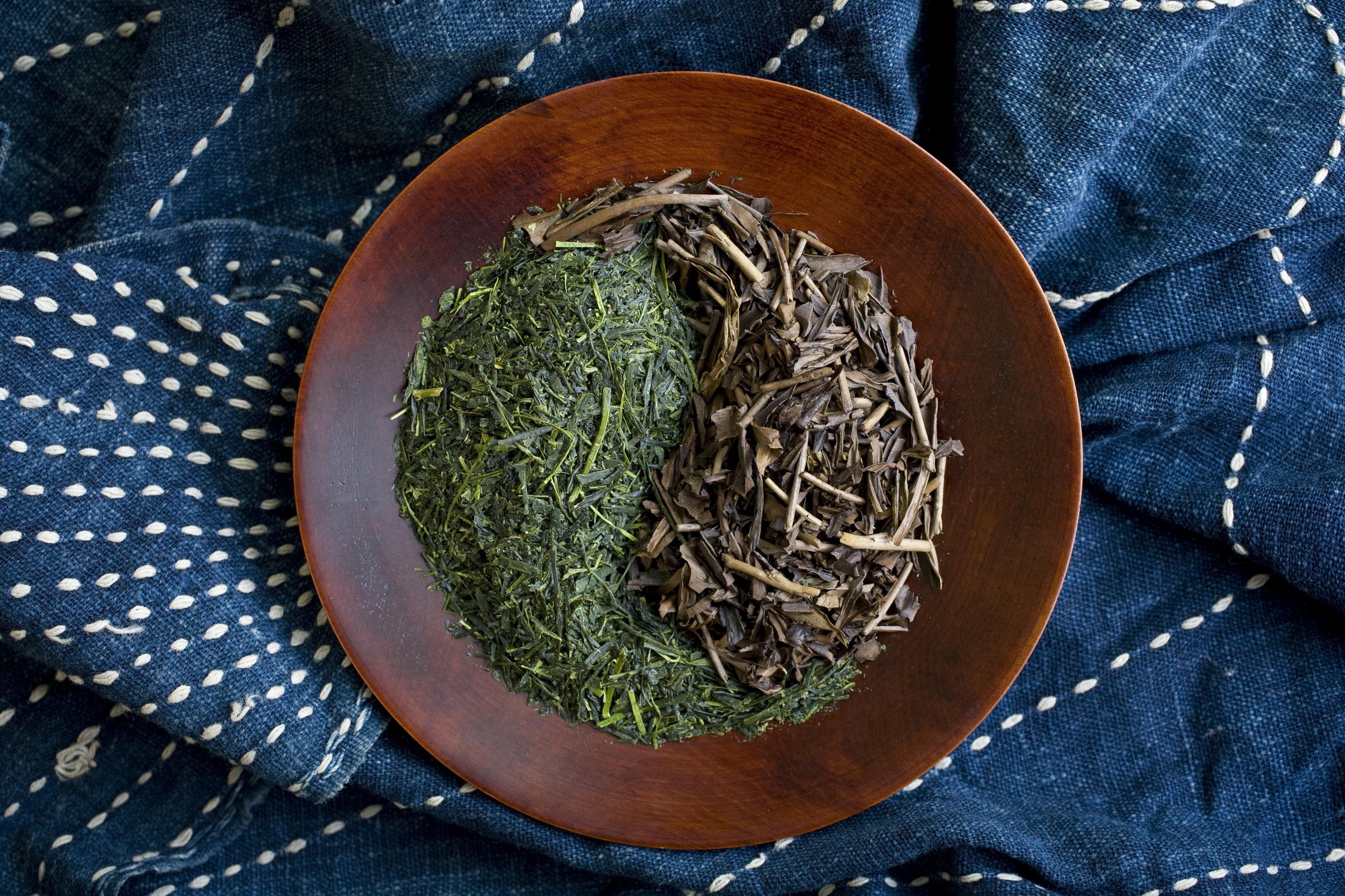 Green tea (sen cha) and hoji cha (roasted tea) in a yin-yang symbol on a cherry bark plate. Vintage aizome (indigo) cloth background.