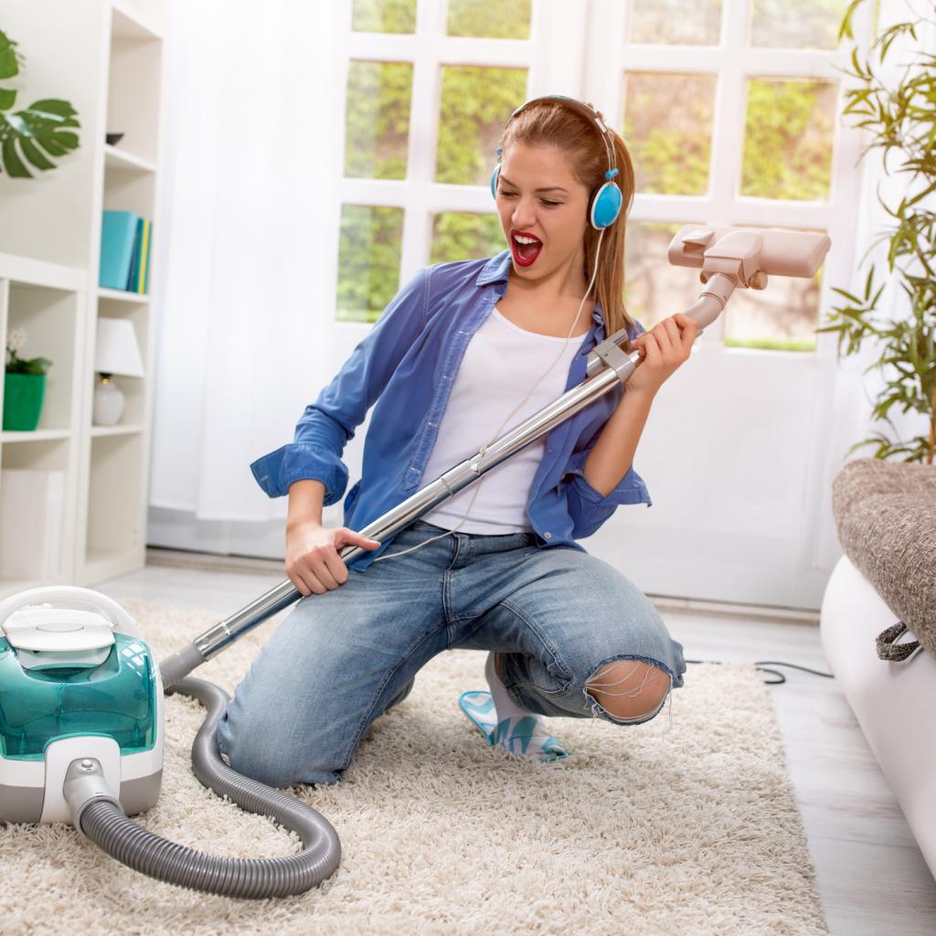 Smiling excited young housewife havig fun with vacuum cleaner