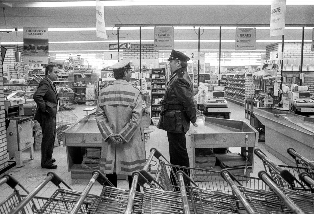 Brute overval op supermarkt Delhaize door De Bende van Nijvel, ook bekend als les Tueurs du Brabant of De dolle schutters van Waals Brabant, is de bekendste criminele organisatie in de Belgische criminele geschiedenis. De laatste overval van de bende is misschien wel de gruwelijkste. Wild schietend komen drie mannen een Delhaize filiaal in Aalst binnen. Daar slaat de paniek toe. Caissières vullen tassen met al het geld en cheques dat ze kunnen vinden. Drie minuten, langer zijn de overvallers niet binnen. Maar dat begint het pas. Ze stappen in hun auto. Een van de overvallers, die inmiddels via getuigenverklaringen de bijnaam de reus heeft gekregen. Zit in de achterbak met een riotgun en vuurt deze onophoudelijk. Wild schiet hij om zich heen, terwijl de auto de parkeerplaats afrijdt. 8 doden vallen er die dag.