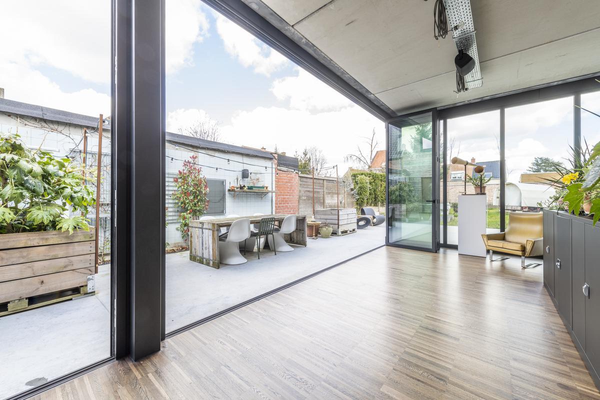 De hele linkerkant van de woonkamer bestaat uit grote harmonicaramen waardoor binnen buiten wordt en het huis in het licht baadt.© Pieter Clicteur