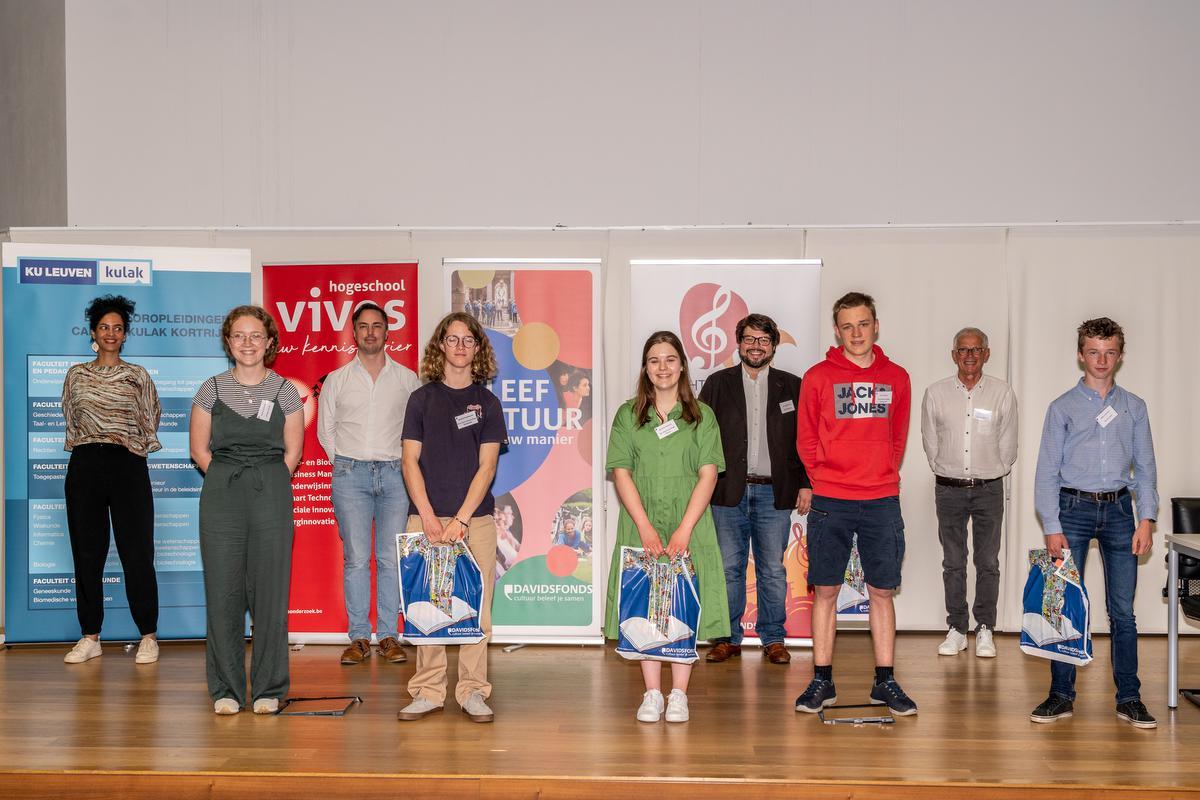 Vooraan zien we de top 5 met v.l.n.r. Paulien Deforche, Martijn Vandeputte, Noortje Heytens, Thor Pieters, Gilles Verbeke. Achteraan staan v.l.n.r. presentatrice Veerle Deblauwe, Broos Debrabander (stichting Aliverde), Kris Opdedrynck, (Algemeen Directeur Davidsfonds), Dirk Debuysere (lid Team Taaltrofee Nederlands).© (Foto KDS)