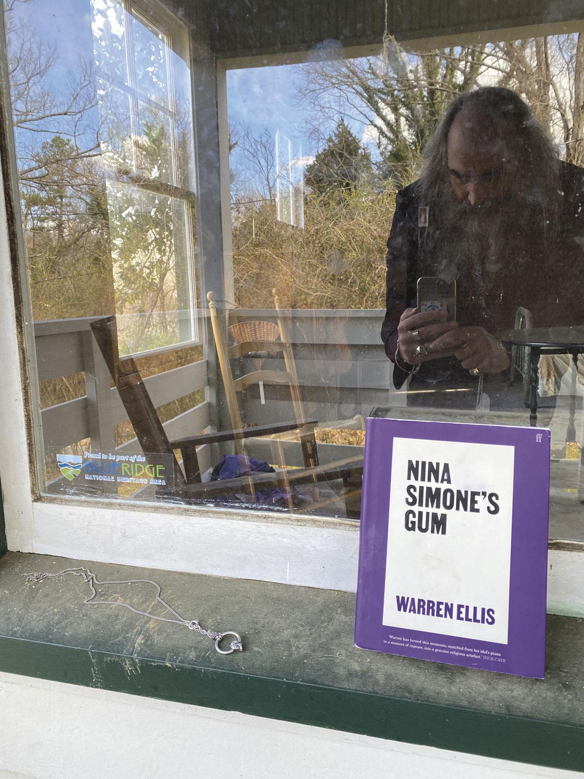 Warren Ellis se prend en photo dans le reflet d'une vitrine de la maison où Nina Simone est née.  Sur le côté, il plaça le pendentif à l'effigie du chewing-gum (réalisé par la styliste flamande Ann Demeulemeester), et le livre qu'il lui dédia.  La boucle est bouclée.