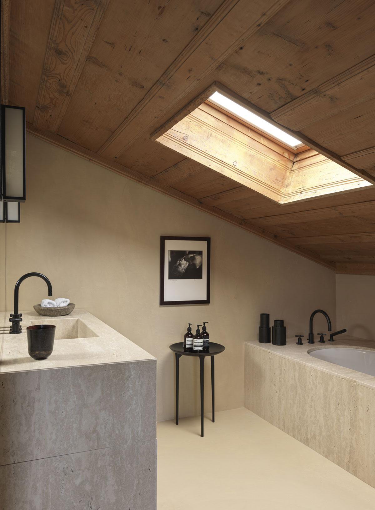 Le travertin contraste avec le bois du plafond en pente dans la salle de bains principale. La photo est signée Leni Riefenstahl.