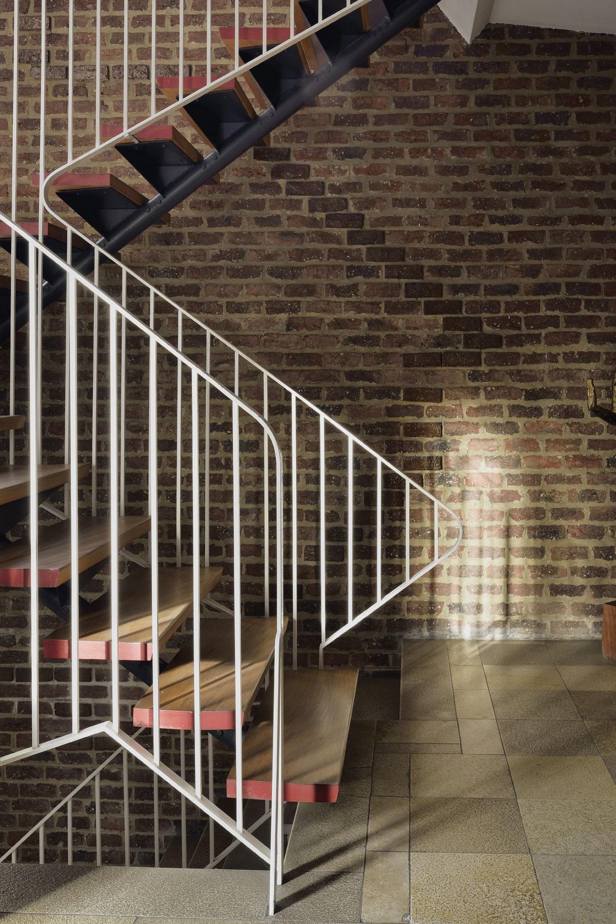 La cage d’escalier ouverte est en briques nues, brutes et texturées. Elles contrastent avec le détail raffiné des contremarches rouge corail de l’escalier suspendu.