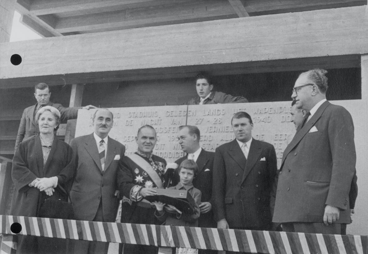 De eerstesteenlegging van het toen nieuwe stadhuis op 8 september 1956, waar ook de hedendaagse foto onderaan werd genomen. We zien v.l.n.r. weduwe Van Coillie, onbekend, burgemeester Adolf Van Glabbeke, Victor Van Coillie, Jan Van Coillie, René Van Coillie, onbekend.