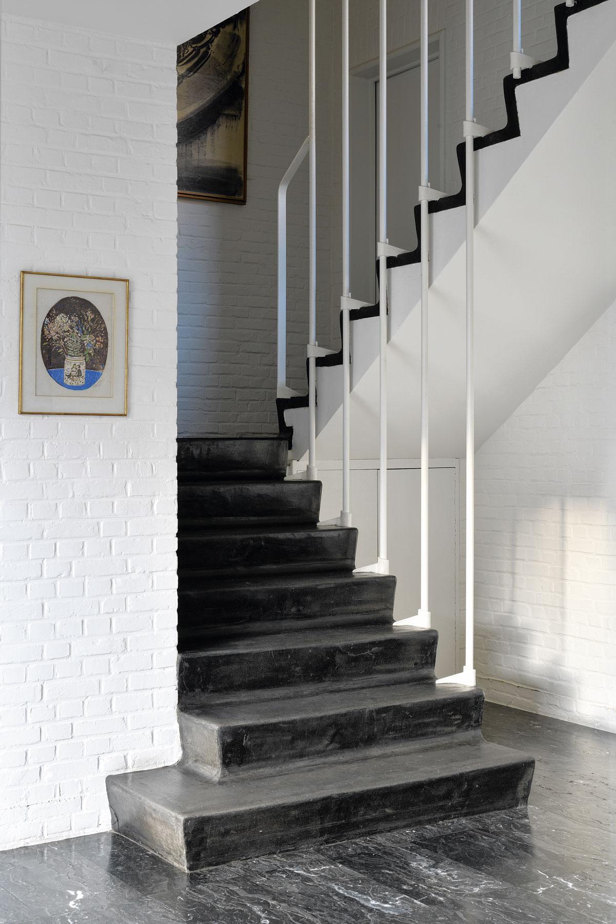 Un beau contraste noir et blanc dans l’entrée: sol en marbre, escalier couvert d’asphalte, et murs en briques peintes en blanc.