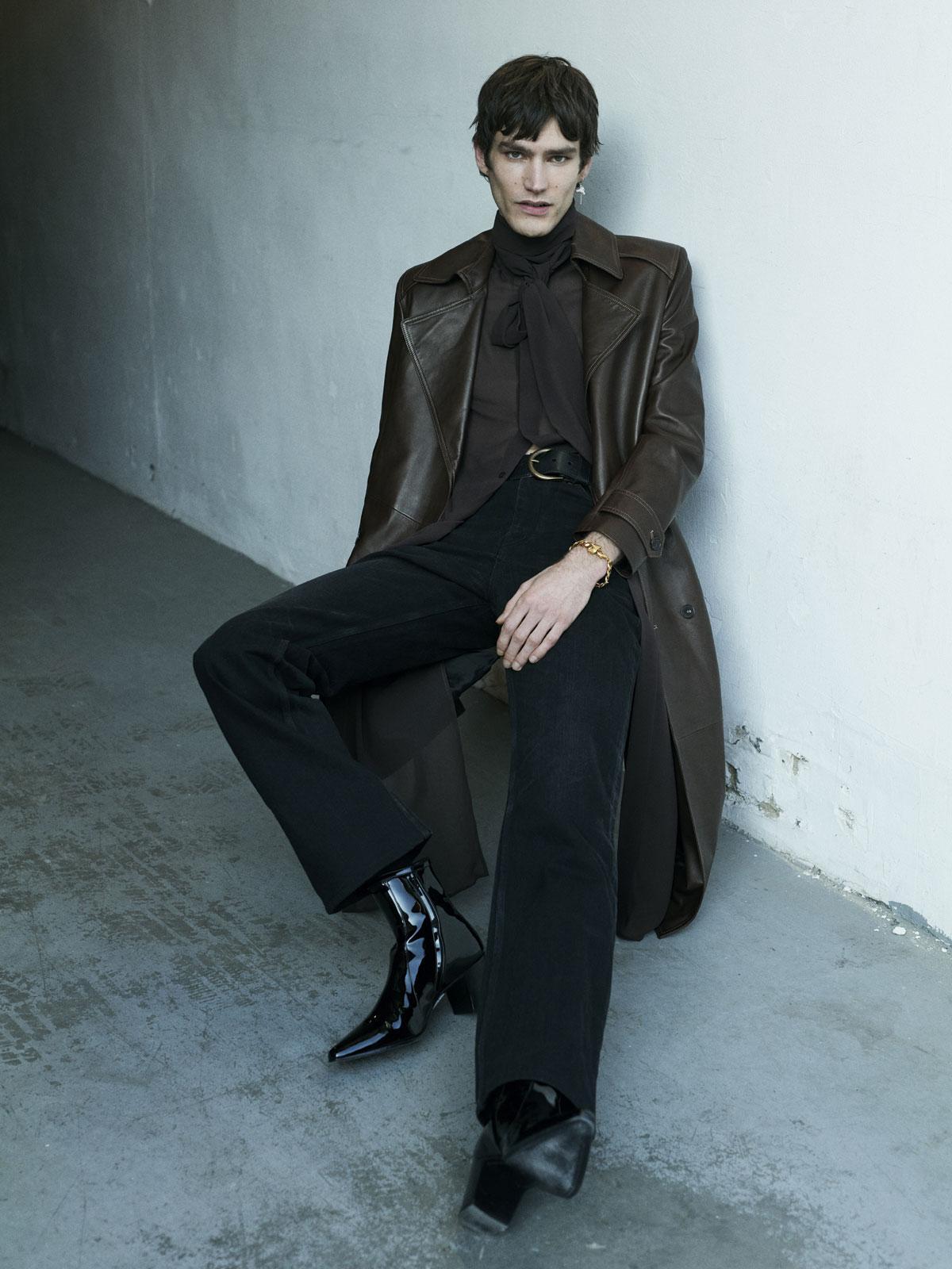 Trench-coat en cuir marron, chemise longue en soie, jeans noir, ceinture en cuir, bottes en cuir verni noir, le tout Saint Laurent. Bijoux, Atelier Elf.