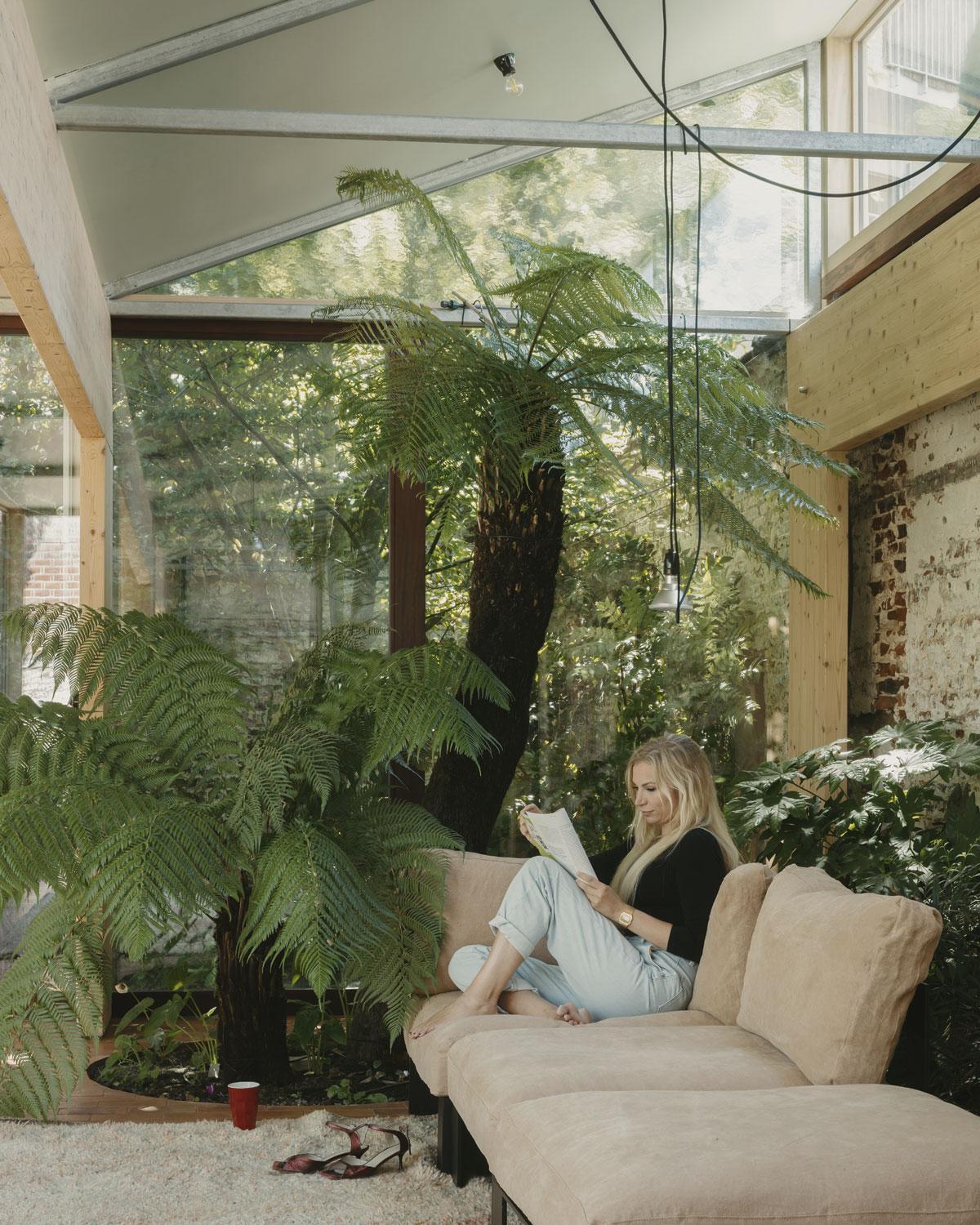 Bewoonster Céline Cousaert naast de boomvaren, in een sofa van Bea Mombaerts voor Serax, tijdens een zeldzaam rustig moment.