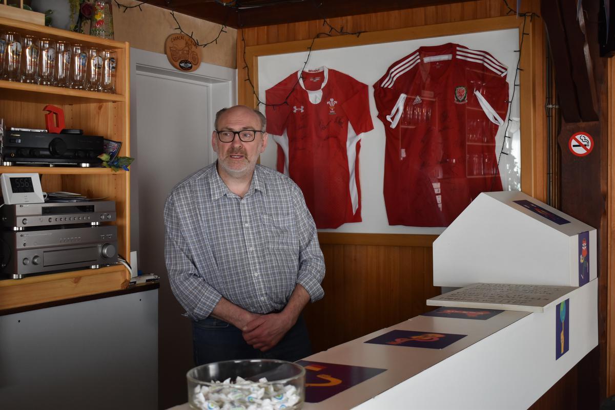 We zien Marc met de ingekaderde en gesigneerde shirts van de nationale voetbalploeg en rugbyploeg van Wales.