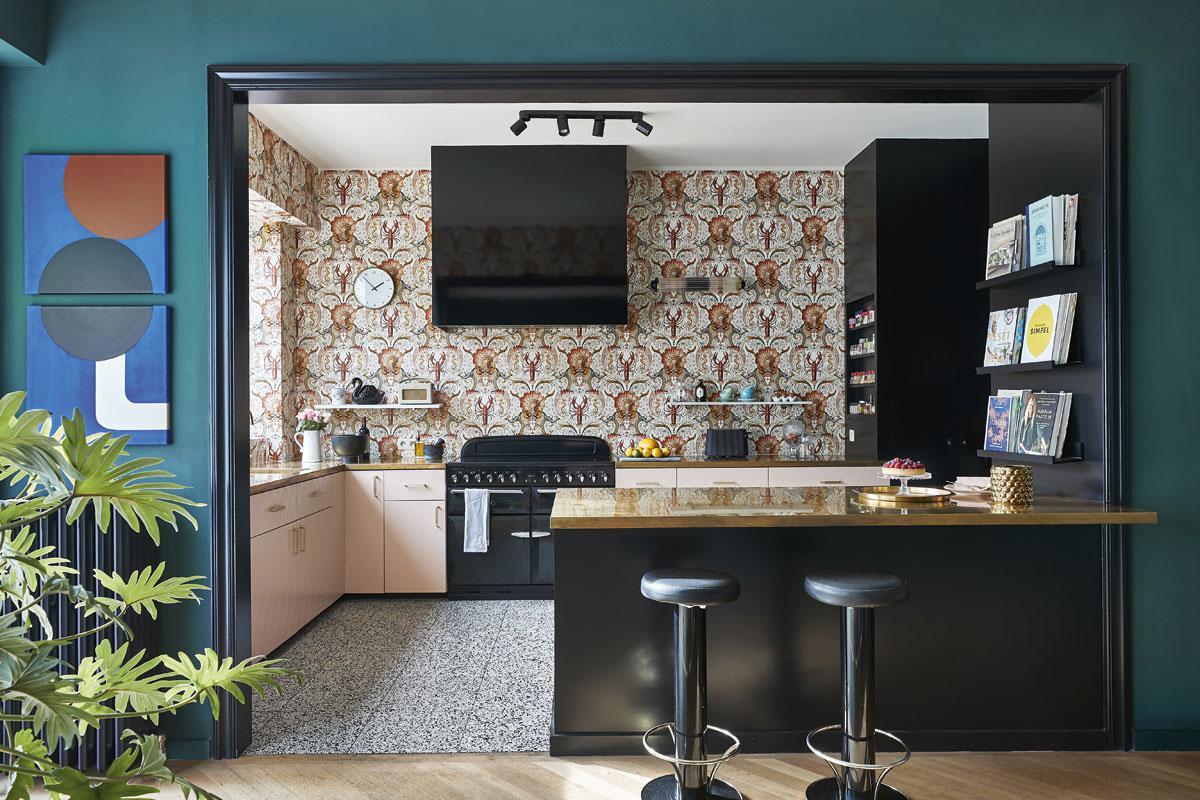 Voor de Ikea-keuken werden nieuwe fronten gemaakt om een klassiekere sfeer te bekomen. Het behangpapier is van Pierre Frey. Het werkblad van de keuken en het eiland zijn in messing. De vintage barkrukken komen van Christiaensen & Christiaensen, het kunstwerk is van Manon Leysen.
