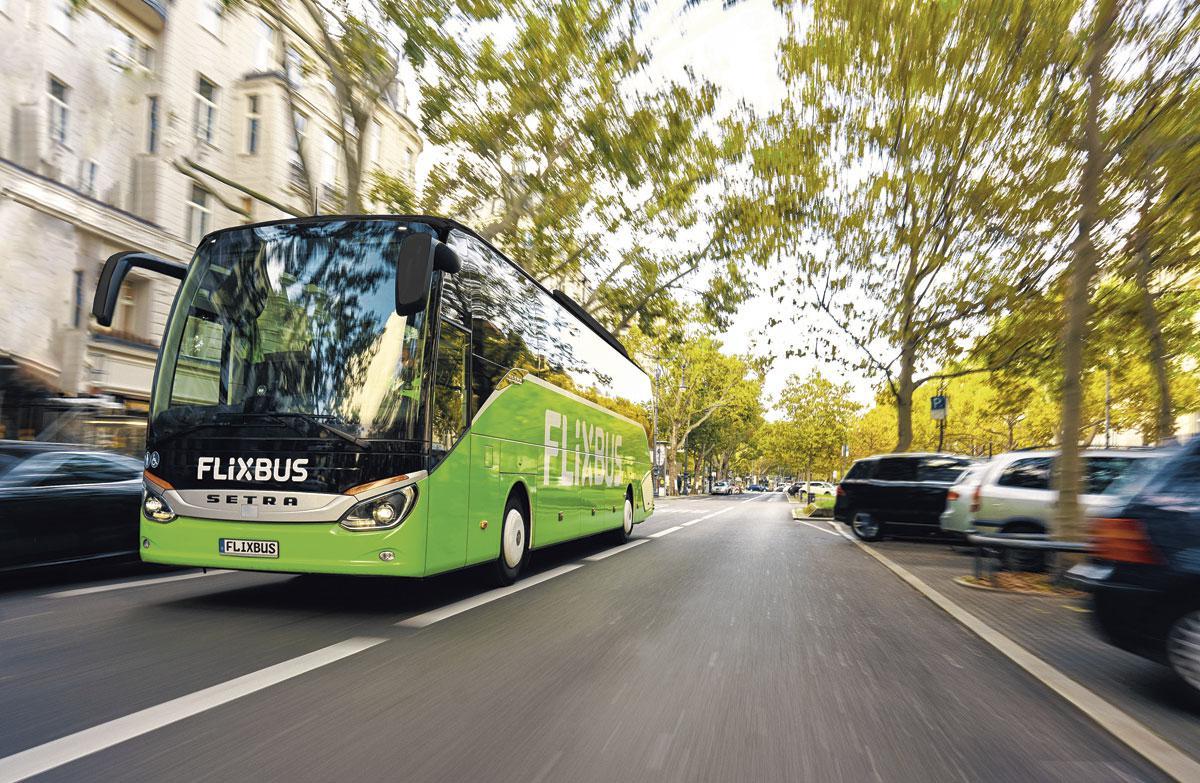 Un des bus verts de FlixBus roulant dans une rue arborée
