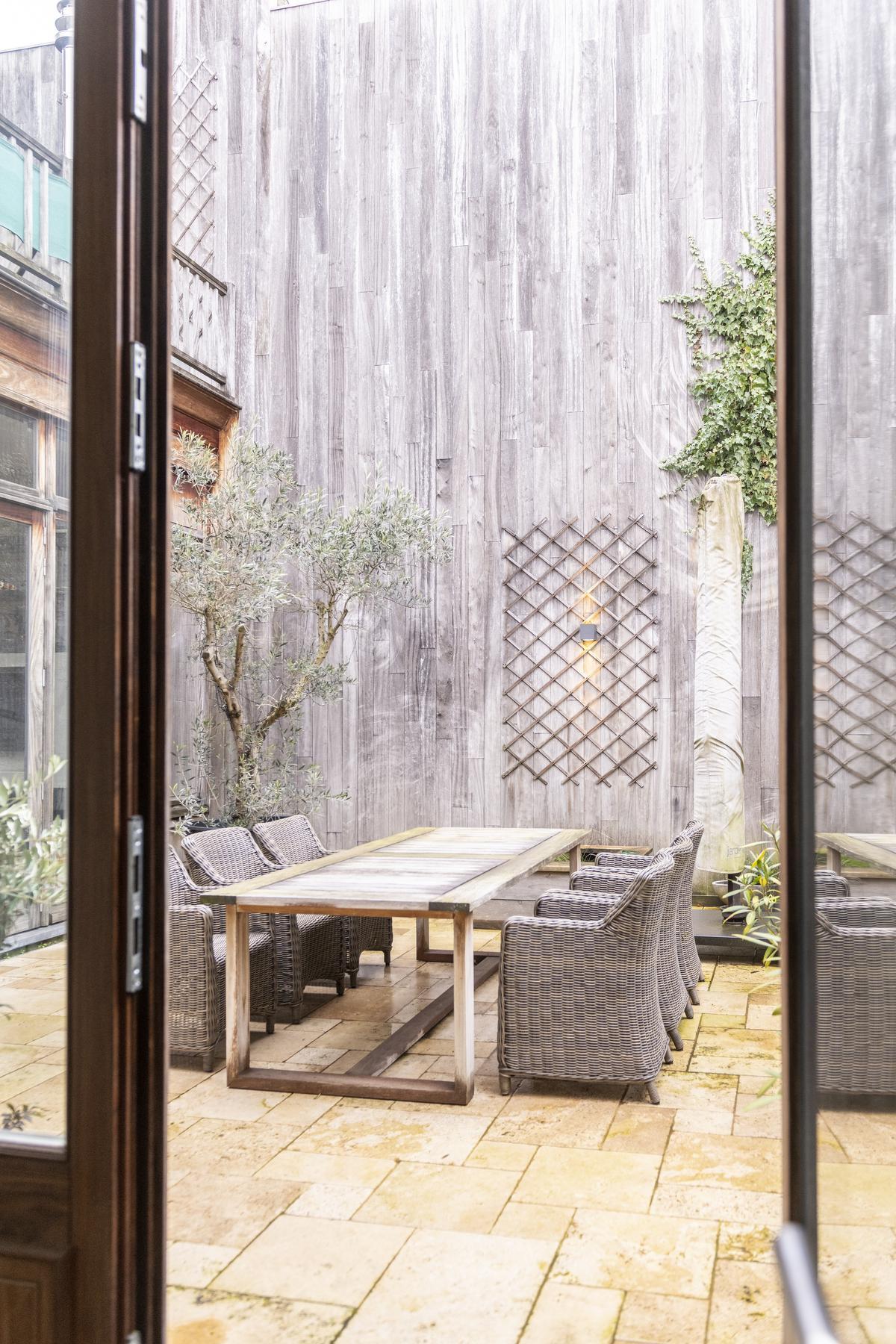 De grote houten ramen in de gezellige woonkamer kijken uit op het terras met olijfboom© Pieter Clicteur