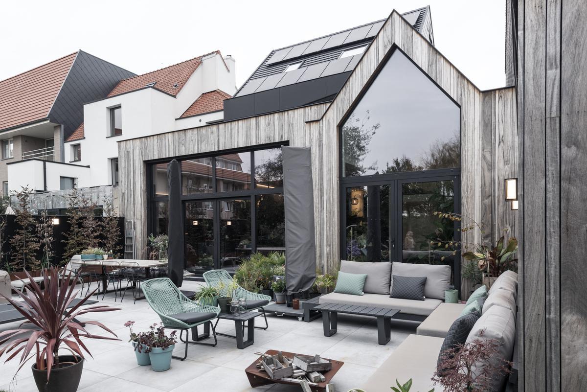Modulaire tuinmeubels van Domus Plus geven karakter aan het terras. De vergrijsde padoek achtergevel en zachtgrijze tegels vergroten het ruimtegevoel met de keuken.© ARG Architecten