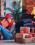 femme assise enlaçant un cadeau de Noël, entourée de paquets sous le sapin