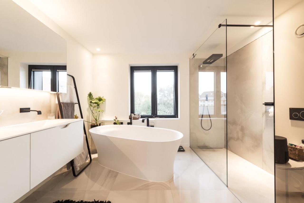 Zongekuste zandtinten en  een glazen doorkijkwand geven de badkamer een onmisbaar wellnessgevoel in huis.©  ARG Architecten