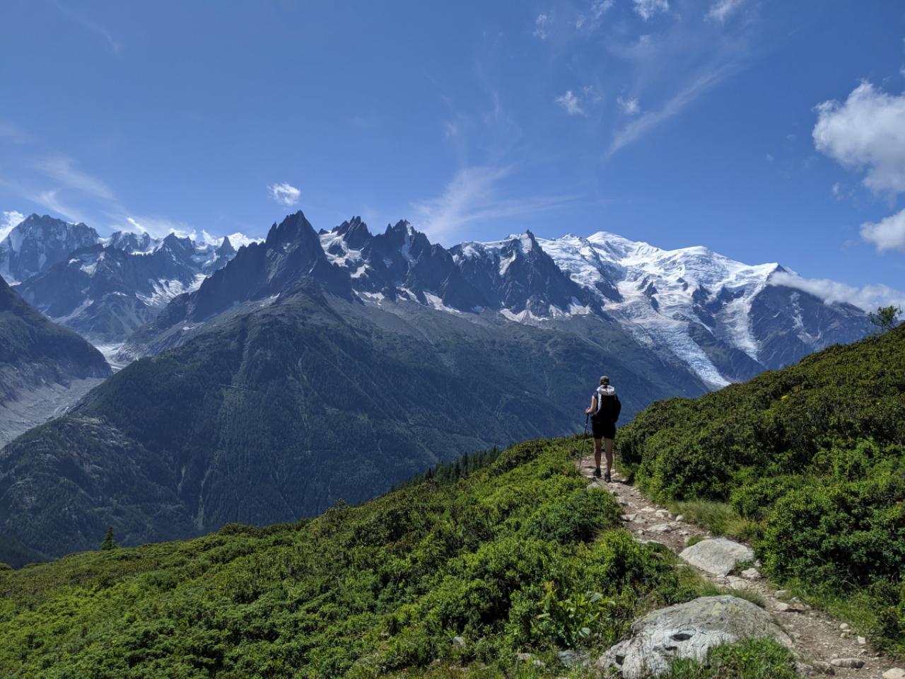A hiker walking on a path during the famous trek Tour du Mont Blanc. Beautiful Alpine view on snowy mountains with blue sky on a sunny morning
