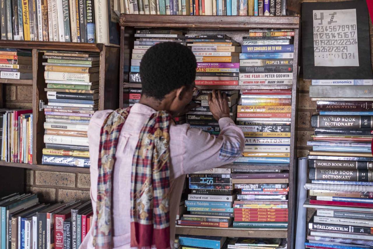 Founder of the Soweto Book Cafe, Thami Mazibuko, pulls a book out of a bookshelf in his home in Soweto on April 5, 2022. - In Thami Mazibuko's childhood home, the 36-year-old has turned the upper level into a bookstore and library, seeded with 30 of his own books, now overflowing with hundreds of donations.
After he finished school, he left Soweto and moved into the formerly white suburbs of Johannesburg, where he stayed with relatives who were artists, with a home full of books.
He developed an insatiable appetite for reading, even bring books into the reggae club where liked to listen to music.
When he decided to move back home, he brought his growing personal collection with him.
So began the Soweto Book Cafe, officially founded in 2018. (Photo by EMMANUEL CROSET / AFP)
