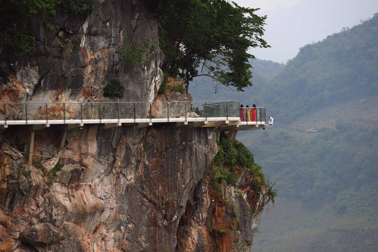 Visitors stand on the walkway section of the Bach Long glass bridge in Moc Chau district in Vietnam's Son La province on April 29, 2022. - Vietnam launched a new attraction for tourists -- with a head for heights -- on April 29 with the opening of a glass-bottomed bridge suspended some 150 metres above a lush, jungle-clad gorge. (Photo by Nhac NGUYEN / AFP)