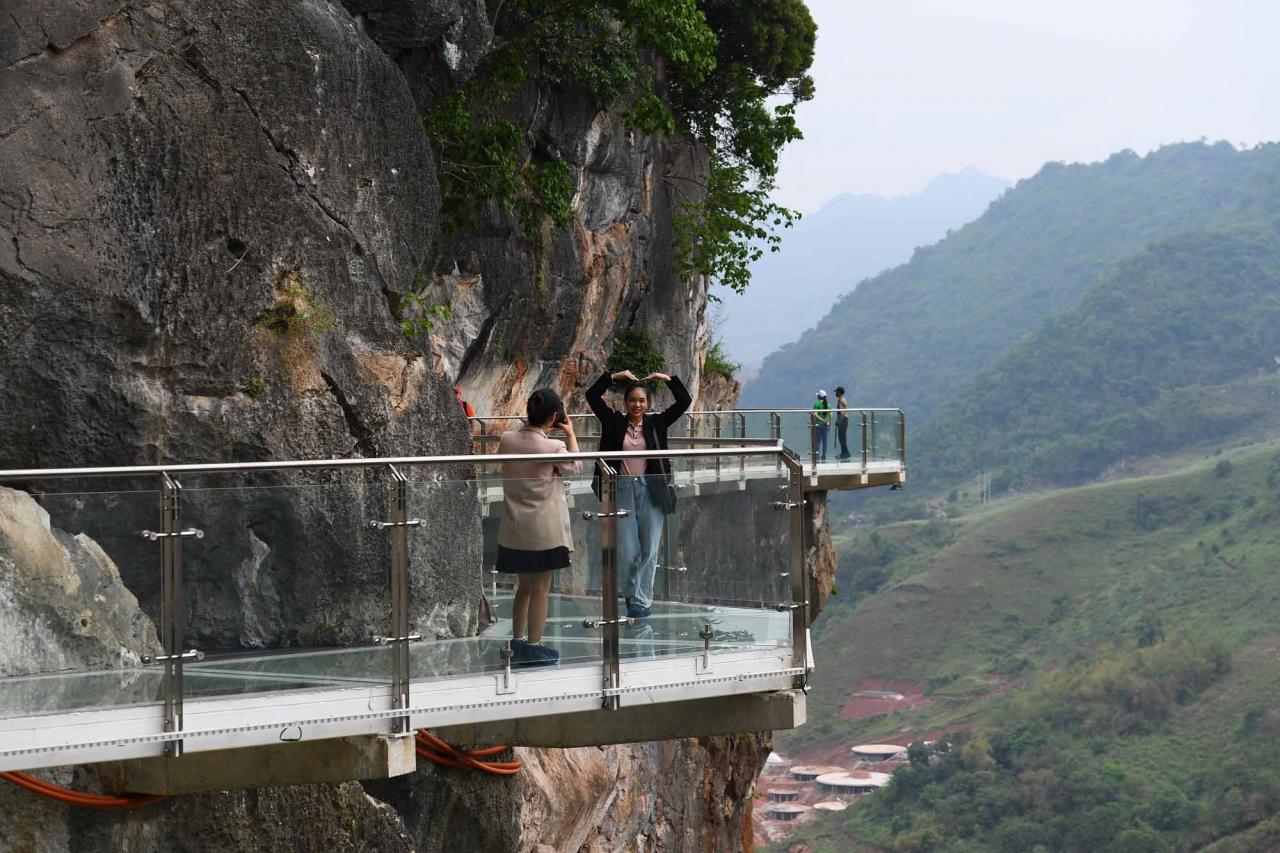 Visitors pose for photos on the walkway section of the Bach Long glass bridge in Moc Chau district in Vietnam's Son La province on April 29, 2022. - Vietnam launched a new attraction for tourists -- with a head for heights -- on April 29 with the opening of a glass-bottomed bridge suspended some 150 metres above a lush, jungle-clad gorge. (Photo by Nhac NGUYEN / AFP)