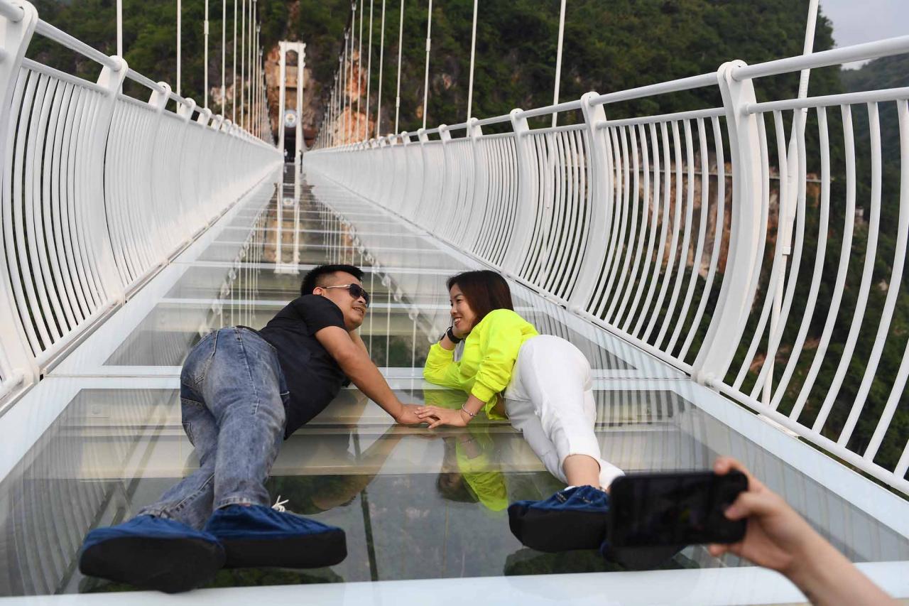 A couple pose for photos on the Bach Long glass bridge in Moc Chau district in Vietnam's Son La province on April 29, 2022. - Vietnam launched a new attraction for tourists -- with a head for heights -- on April 29 with the opening of a glass-bottomed bridge suspended some 150 metres above a lush, jungle-clad gorge. (Photo by Nhac NGUYEN / AFP)