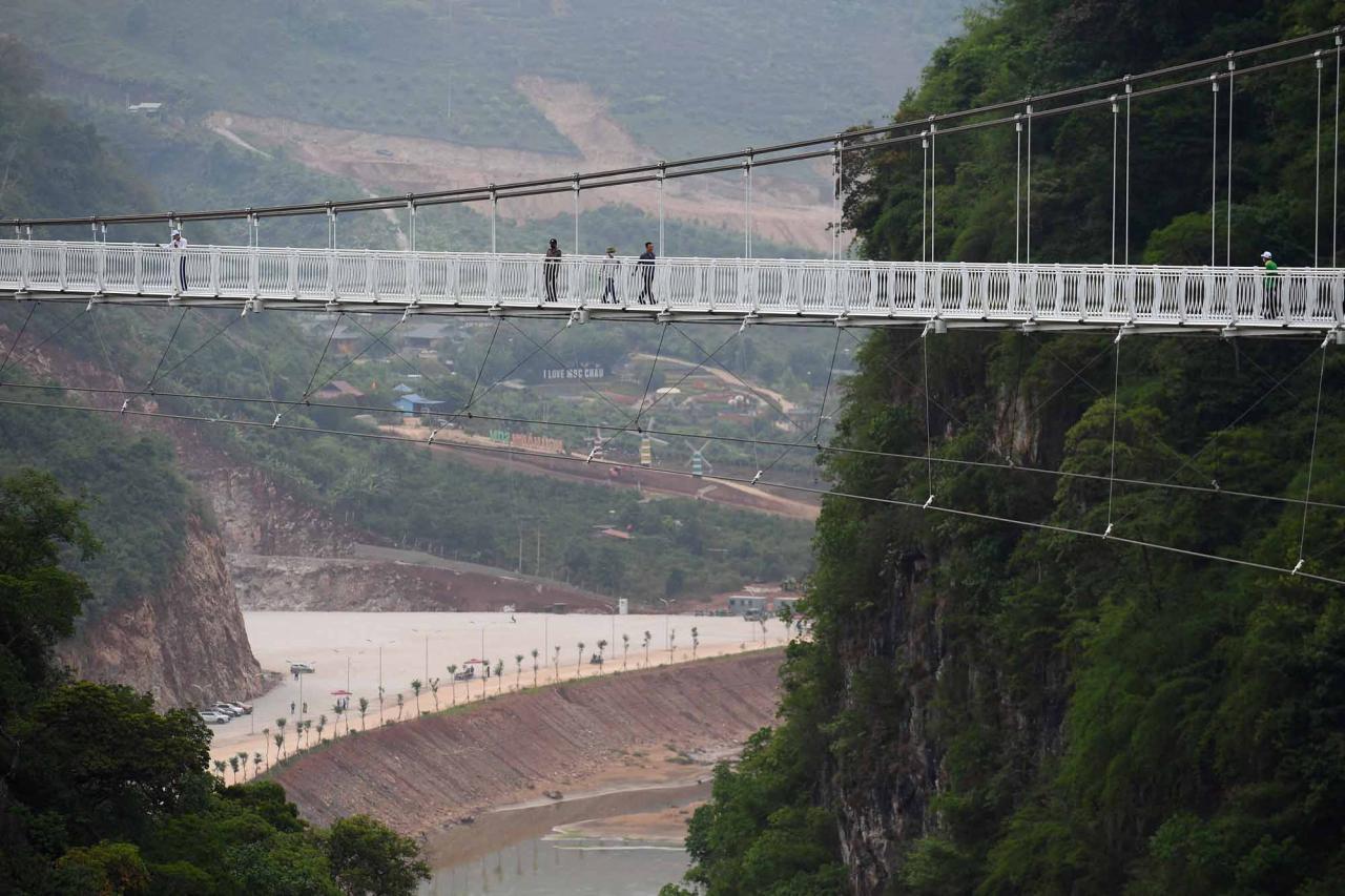 Visitors walk on the Bach Long glass bridge in Moc Chau district in Vietnam's Son La province on April 29, 2022. - Vietnam launched a new attraction for tourists -- with a head for heights -- on April 29 with the opening of a glass-bottomed bridge suspended some 150 metres above a lush, jungle-clad gorge. (Photo by Nhac NGUYEN / AFP)