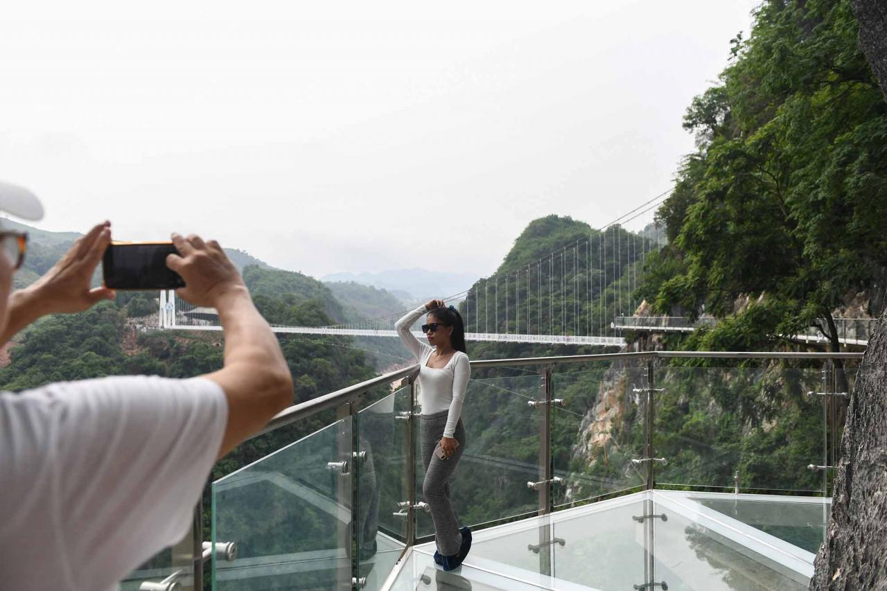 A visitor poses for photos on the walkway section of the Bach Long glass bridge in Moc Chau district in Vietnam's Son La province on April 29, 2022. - Vietnam launched a new attraction for tourists -- with a head for heights -- on April 29 with the opening of a glass-bottomed bridge suspended some 150 metres above a lush, jungle-clad gorge. (Photo by Nhac NGUYEN / AFP)
