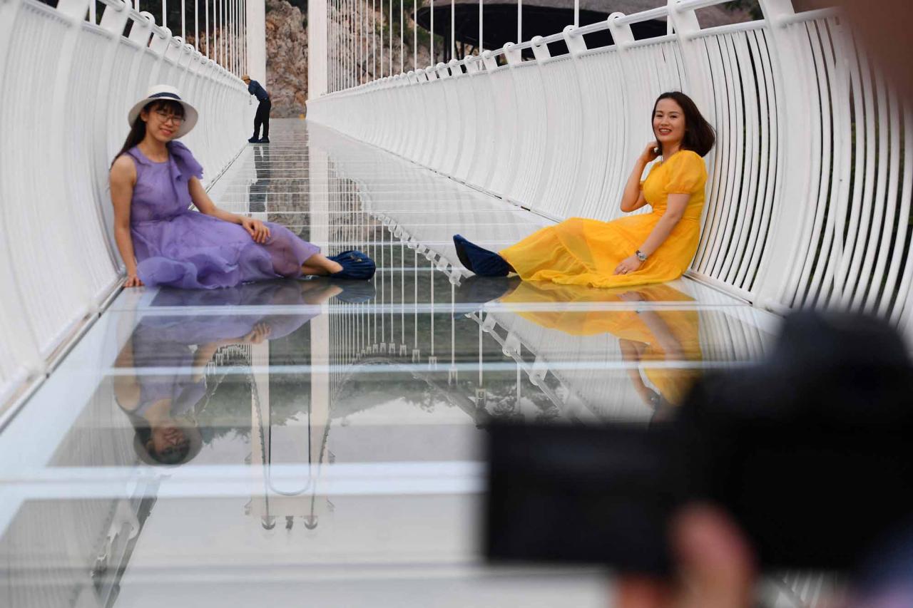 This photo taken on April 28, 2022 shows visitors posing for photos on the Bach Long glass bridge in Moc Chau district in Vietnam's Son La province. - Vietnam launched a new attraction for tourists -- with a head for heights -- on April 29 with the opening of a glass-bottomed bridge suspended some 150 metres above a lush, jungle-clad gorge. (Photo by Nhac NGUYEN / AFP)