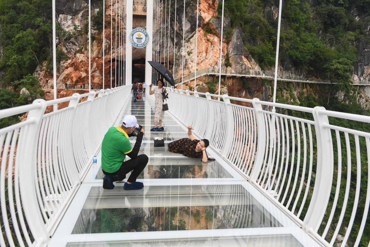Visitors pose for photos on the Bach Long glass bridge in Moc Chau district in Vietnam's Son La province on April 29, 2022. - Vietnam launched a new attraction for tourists -- with a head for heights -- on April 29 with the opening of a glass-bottomed bridge suspended some 150 metres above a lush, jungle-clad gorge. (Photo by Nhac NGUYEN / AFP)