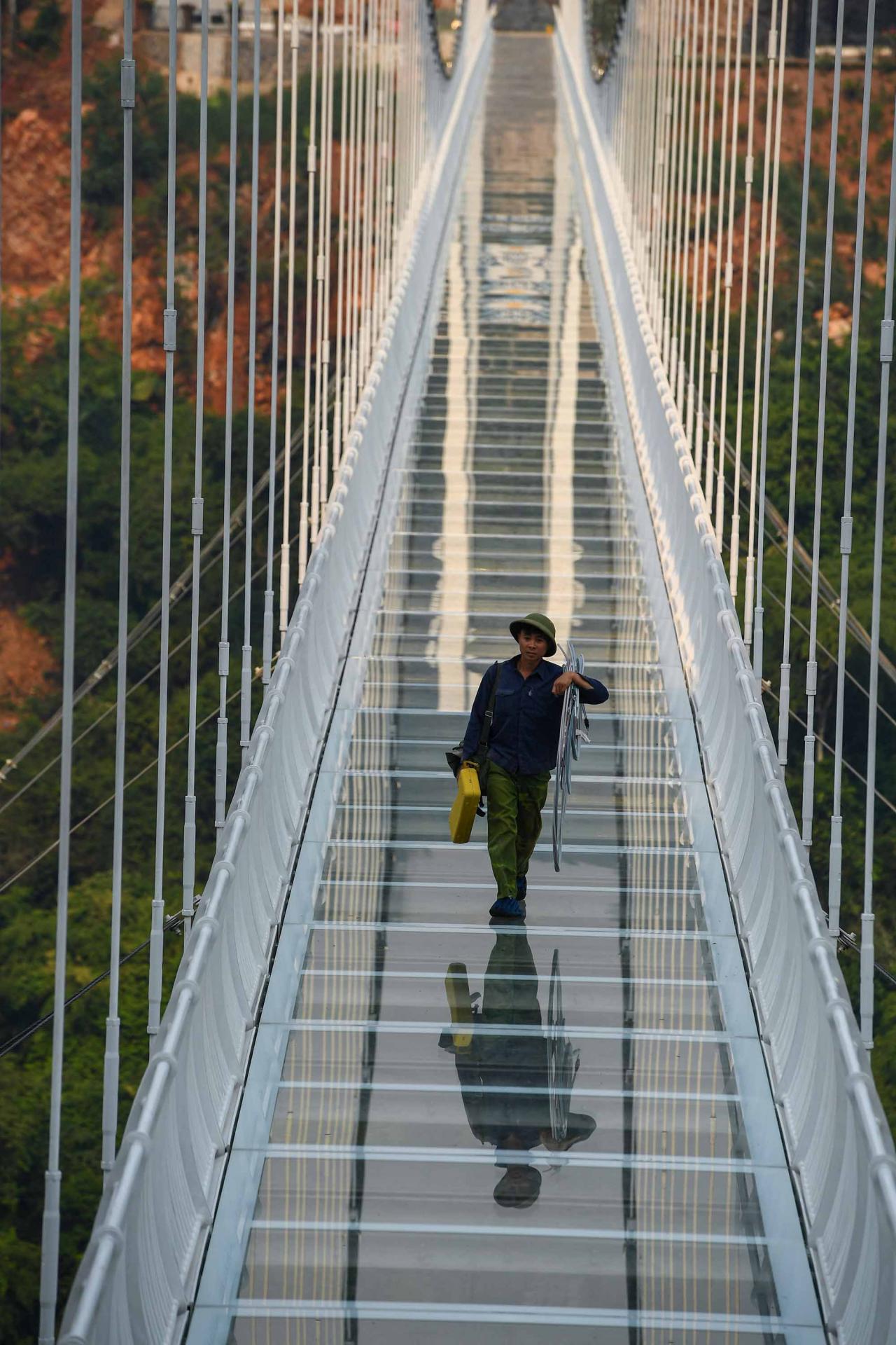 This photo taken on April 28, 2022 shows a worker walking on the Bach Long glass bridge in Moc Chau district in Vietnam's Son La province. - Vietnam launched a new attraction for tourists -- with a head for heights -- on April 29 with the opening of a glass-bottomed bridge suspended some 150 metres above a lush, jungle-clad gorge. (Photo by Nhac NGUYEN / AFP)
