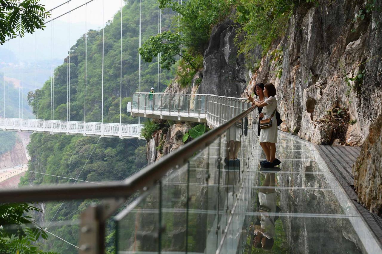 Visitors stand on the walkway section of the Bach Long glass bridge in Moc Chau district in Vietnam's Son La province on April 29, 2022. - Vietnam launched a new attraction for tourists -- with a head for heights -- on April 29 with the opening of a glass-bottomed bridge suspended some 150 metres above a lush, jungle-clad gorge. (Photo by Nhac NGUYEN / AFP)