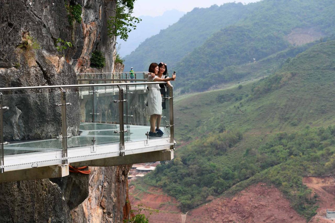Visitors take photos on the walkway section of the Bach Long glass bridge in Moc Chau district in Vietnam's Son La province on April 29, 2022. - Vietnam launched a new attraction for tourists -- with a head for heights -- on April 29 with the opening of a glass-bottomed bridge suspended some 150 metres above a lush, jungle-clad gorge. (Photo by Nhac NGUYEN / AFP)