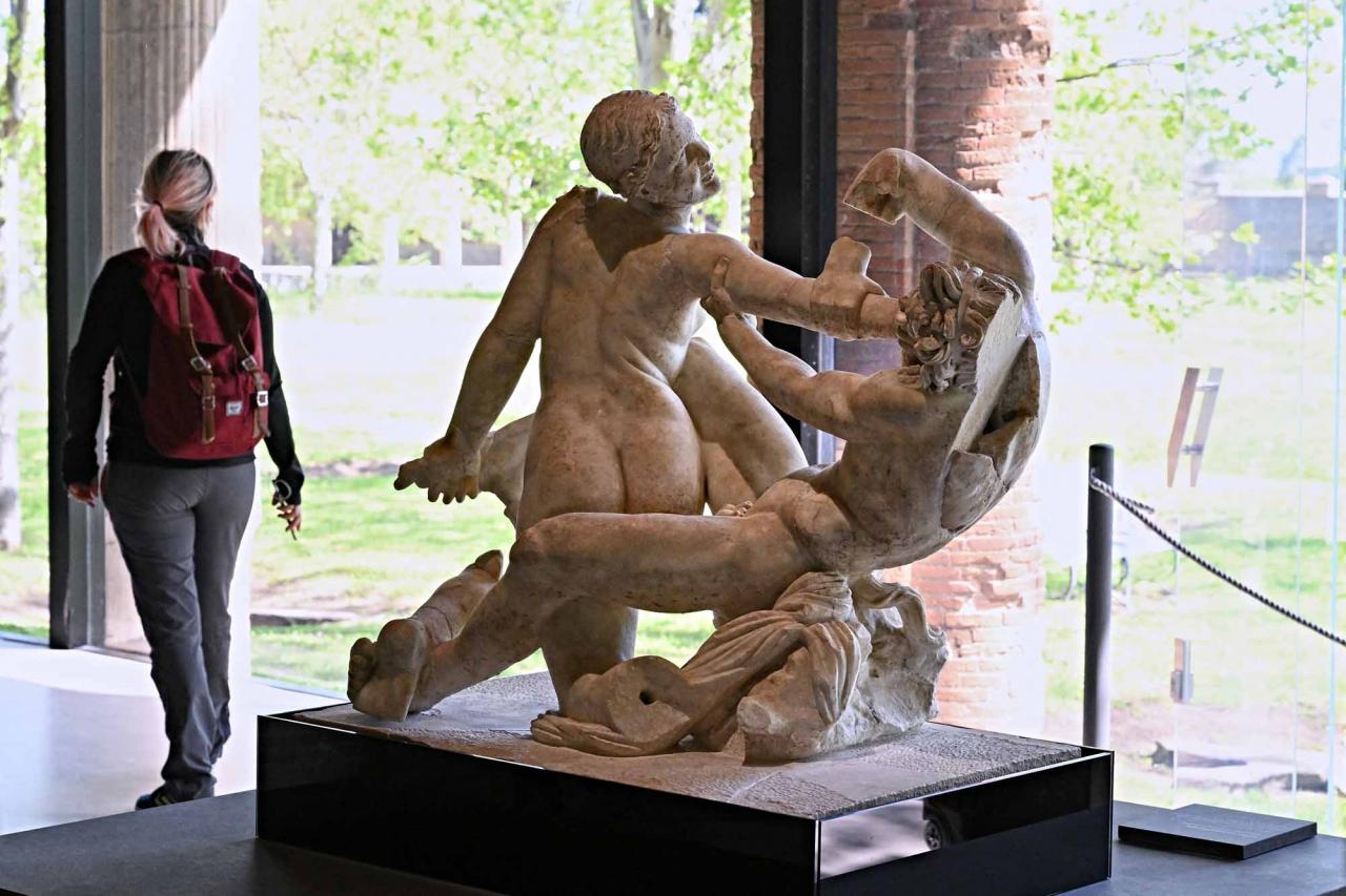 A vistor walks next to a "Satyr and hermaphrodite" sculpture, in Pompeii's site of a new exhibition entitled "Art and sensuality in the houses of Pompeii" on art and sexuality in the ancient city, where sculptures and paintings of breasts and buttocks abounded, on April 28, 2022. - Raunchy scenes may redden faces at a new exhibition in Pompeii on art and sexuality in the ancient Roman city, where sculptures and paintings of breasts and buttocks abounded. Archaeologists excavating the city, which was destroyed by the eruption of nearby Vesuvius in 79 AD, were initially startled to discover erotic images everywhere, from garden statues to ceiling frescos. (Photo by Andreas SOLARO / AFP)