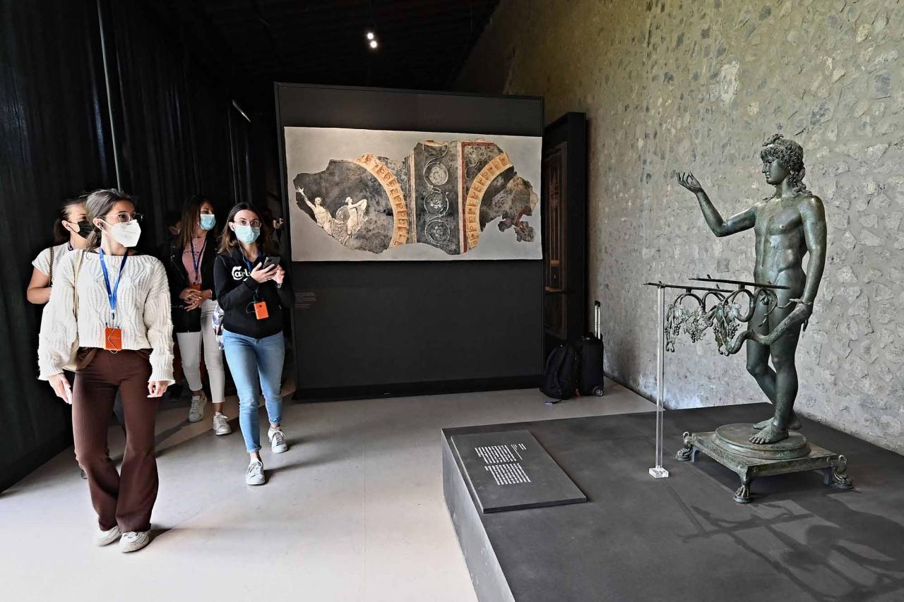 Visitors look at a sculpture of Ephebe lamp-holder, in Pompeii's site during a new exhibition entitled "Art and sensuality in the houses of Pompeii" on art and sexuality in the ancient city, where sculptures and paintings of breasts and buttocks abounded, on April 28, 2022. - Raunchy scenes may redden faces at a new exhibition in Pompeii on art and sexuality in the ancient Roman city, where sculptures and paintings of breasts and buttocks abounded. Archaeologists excavating the city, which was destroyed by the eruption of nearby Vesuvius in 79 AD, were initially startled to discover erotic images everywhere, from garden statues to ceiling frescos. (Photo by Andreas SOLARO / AFP)