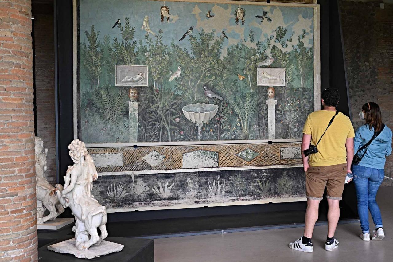Visitors look at a "Wall with lush garden of a large reception room" fresco, during a new exhibition in Pompeii's site entitled "Art and sensuality in the houses of Pompeii" on art and sexuality in the ancient city, where sculptures and paintings of breasts and buttocks abounded, on April 28, 2022. - Raunchy scenes may redden faces at a new exhibition in Pompeii on art and sexuality in the ancient Roman city, where sculptures and paintings of breasts and buttocks abounded. Archaeologists excavating the city, which was destroyed by the eruption of nearby Vesuvius in 79 AD, were initially startled to discover erotic images everywhere, from garden statues to ceiling frescos. (Photo by Andreas SOLARO / AFP)