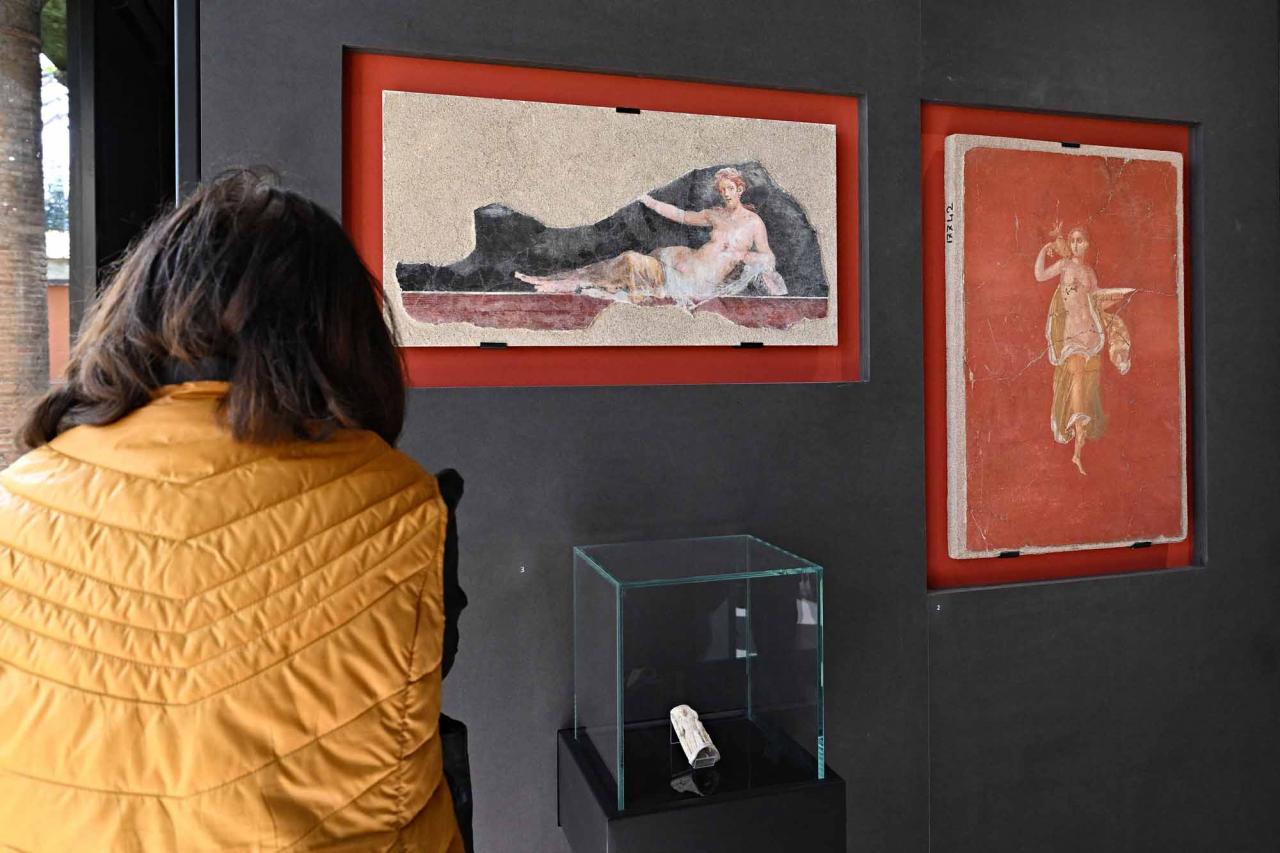 A visitor looks on during a new exhibition in Pompeii's site entitled "Art and sensuality in the houses of Pompeii" on art and sexuality in the ancient city, where sculptures and paintings of breasts and buttocks abounded, on April 28, 2022. - Raunchy scenes may redden faces at a new exhibition in Pompeii on art and sexuality in the ancient Roman city, where sculptures and paintings of breasts and buttocks abounded. Archaeologists excavating the city, which was destroyed by the eruption of nearby Vesuvius in 79 AD, were initially startled to discover erotic images everywhere, from garden statues to ceiling frescos. (Photo by Andreas SOLARO / AFP)