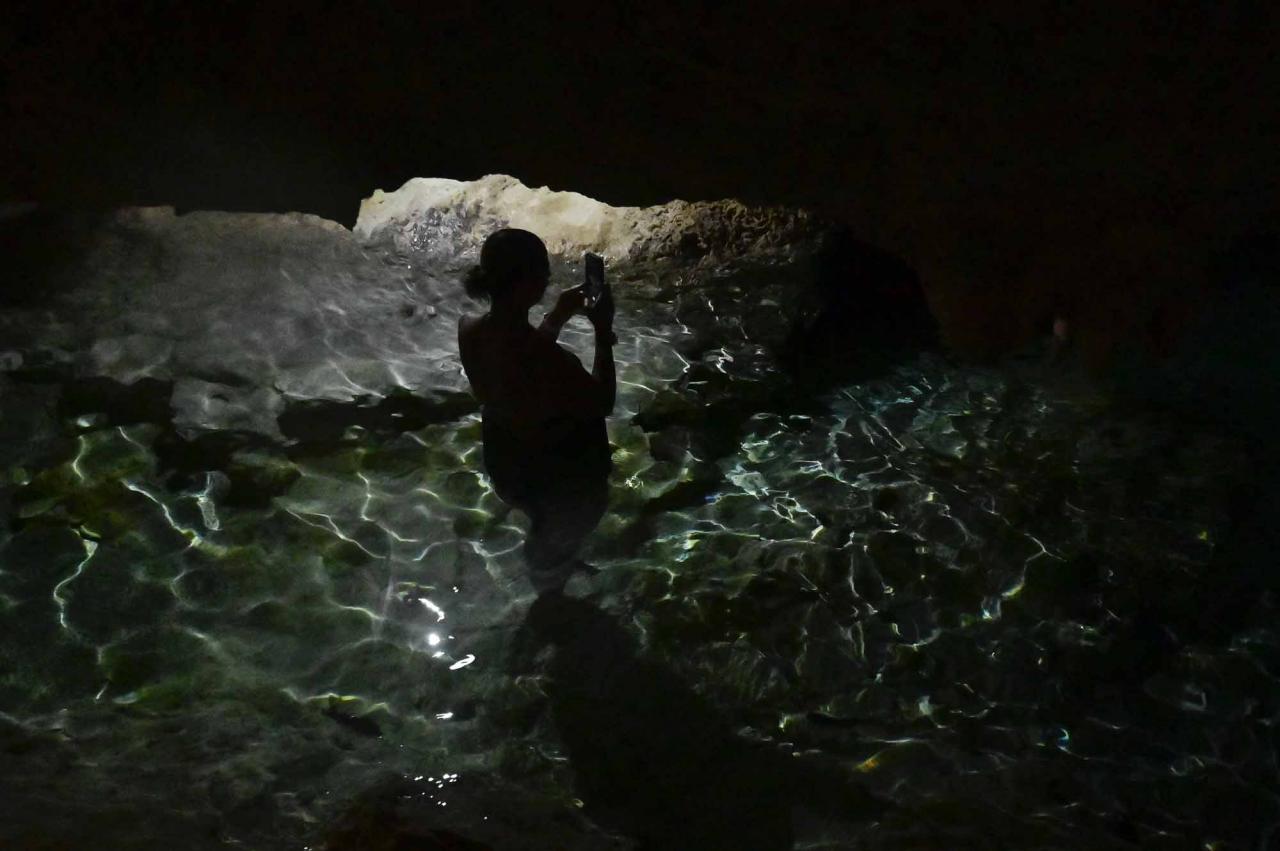 A tourist takes a picture in a water-filled sinkhole known as cenote at Aktun Chen natural park, near the construction site of Section 5 South of the Mayan Train between the resorts of Playa del Carmen and Tulum which was halted by a district judge pending resolution of an injunction sought by scuba divers and environmentalists -- in Akumal, Tulum, Quintana Roo State, Mexico, on April 27, 2022. - A Mexican judge earlier this month suspended construction of part of President Andres Manuel Lopez Obrador's flagship tourist train project in the Yucatan peninsula due to a lack of environmental impact studies. The Mayan Train, a roughly 1,500-kilometre (950 mile) rail loop linking popular Caribbean beach resorts and archeological ruins, has met with opposition from environmentalists and indigenous communities. (Photo by Pedro PARDO / AFP)