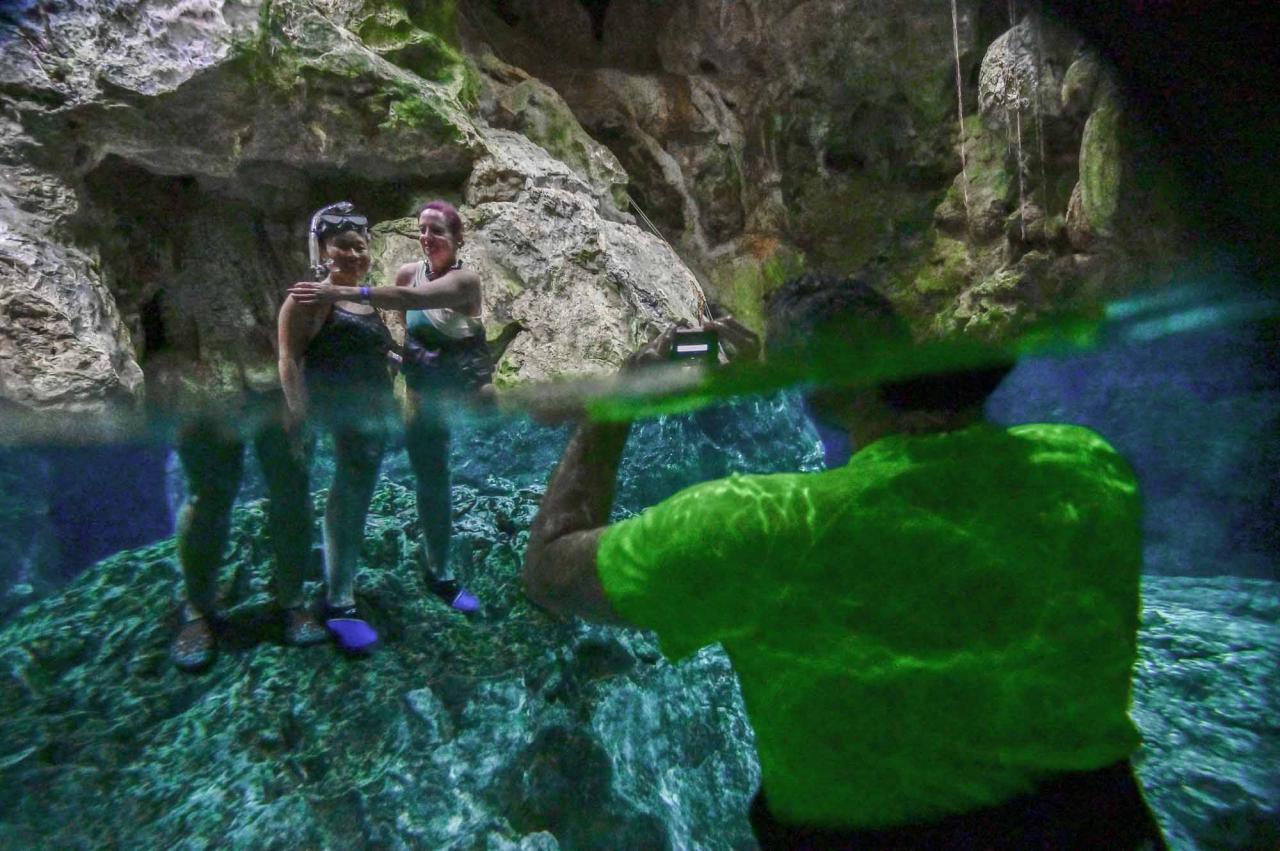 Tourists pose for a picture in a water-filled sinkhole known as cenote at Aktun Chen natural park, near the construction site of Section 5 South of the Mayan Train between the resorts of Playa del Carmen and Tulum which was halted by a district judge pending resolution of an injunction sought by scuba divers and environmentalists -- in Akumal, Tulum, Quintana Roo State, Mexico, on April 27, 2022. - A Mexican judge earlier this month suspended construction of part of President Andres Manuel Lopez Obrador's flagship tourist train project in the Yucatan peninsula due to a lack of environmental impact studies. The Mayan Train, a roughly 1,500-kilometre (950 mile) rail loop linking popular Caribbean beach resorts and archeological ruins, has met with opposition from environmentalists and indigenous communities. (Photo by Pedro PARDO / AFP)